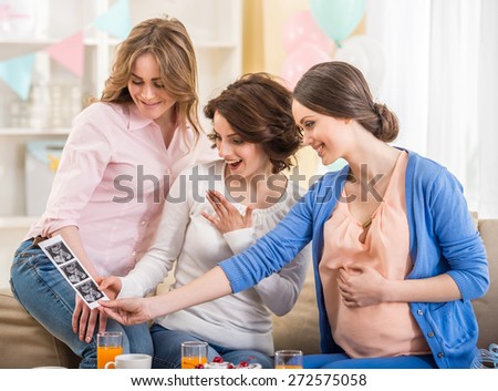 Women is visiting pregnant friend at home. They are looking at  x-ray image of baby.