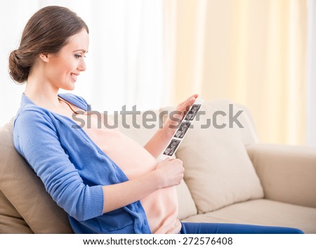 Side view of beautiful pregnant woman sitting on the chair and holding x-ray image of her baby.