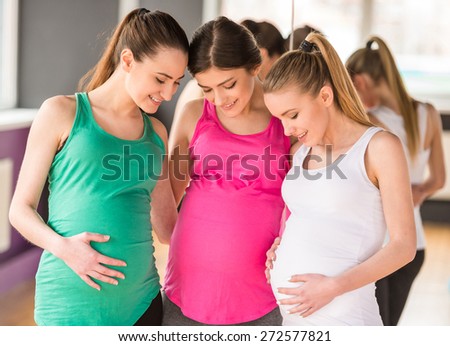 Happy pregnant women are looking at their bellies.