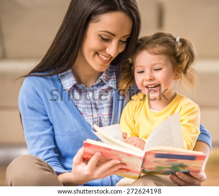 Charming mother is showing images in a book to her cute little daughter at home.