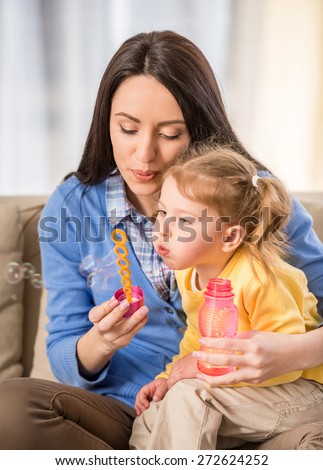 Beautiful young mother together with her daughter making soap bubbles.