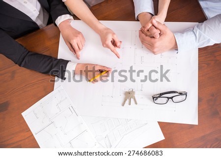 Female realtor showing contract with floor layout in an apartment to a young couple. Close-up.