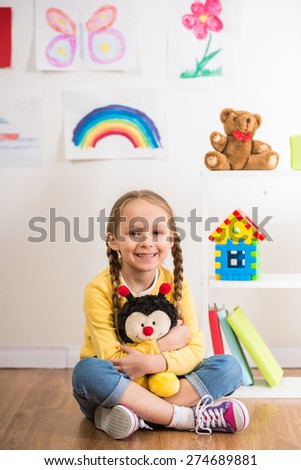 Little pretty smiling girl in yellow  pullover  holding toy bee on colorful background.