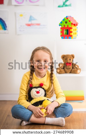 Little pretty smiling girl in yellow  pullover  playing with toy bee on colorful background.