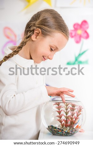Little pretty  smiling girl in white  pullover  playing with gold fish in aquarium on colorful background.