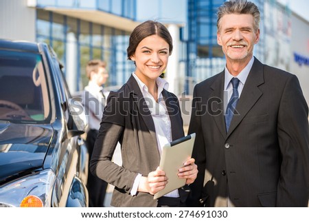 Two  successful confident businesspeople in suits   at a meeting  standing near car.