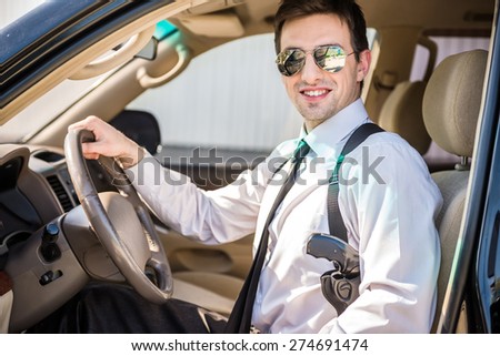Young confident smiling businessman  in sunglasses with gun sitting in his luxurious car.
