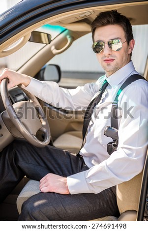 Young confident  businessman  in sunglasses with gun sitting in his luxurious car.