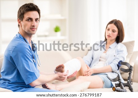 Young handsome male doctor with stethoscope examining leg of female patient.