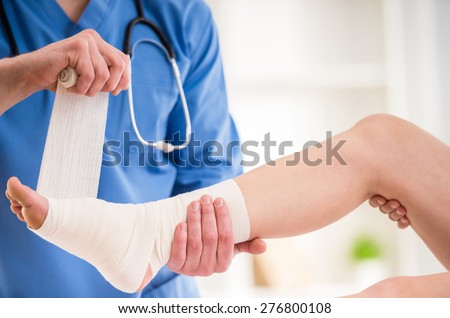 Close-up of male doctor bandaging  foot of female patient at doctor\'s office.