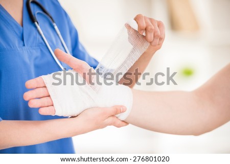 Close-up of female doctor with stethoscope  bandaging hand of male patient.