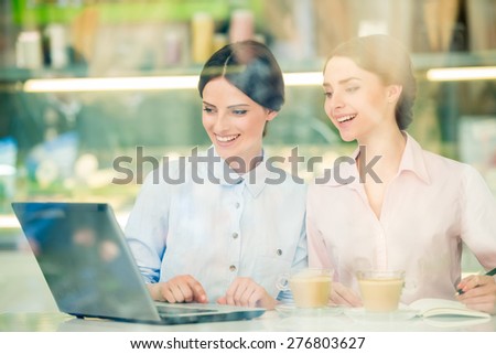 Two young beautiful businesswomen  sitting in urban cafe and using laptop.
