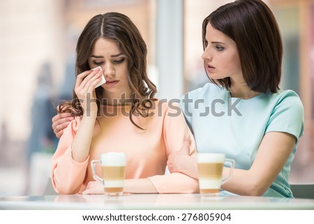 Young girl talking with her upset friend and holding her shoulders in cafe.