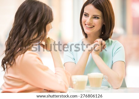 Two young beautiful girls sitting in urban cafe with coffee and sharing secrets.