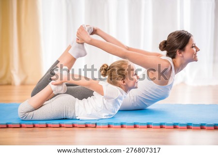 Mother and daughter doing yoga exercises on rug at home.