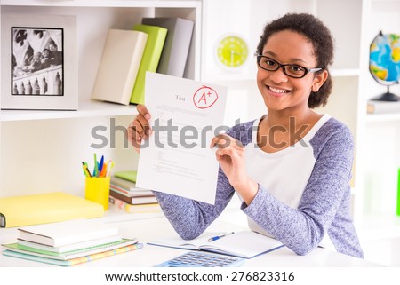 Young schoolgirl  in glasses sitting at the table and  showing perfect test results on colorful background.