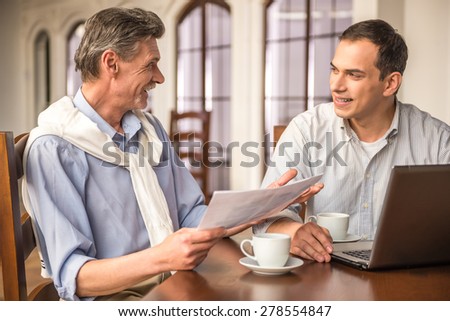 Two handsome businessmen in shirts sitting at the wooden table in urban cafe and using laptop.