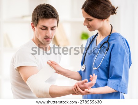 Young attractive female doctor with stethoscope  bandaging hand of male patient.
