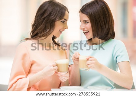 Two young beautiful girls sitting in urban cafe with coffee and sharing secrets.