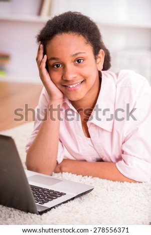 Young pretty schoolgirl laying on the carpet and using laptop.