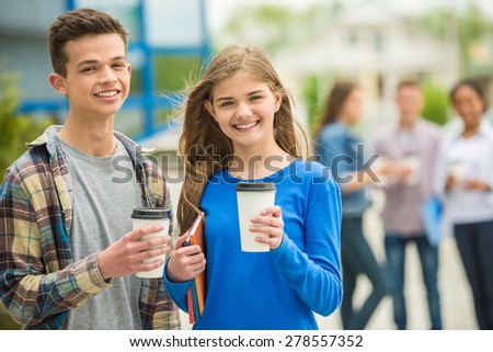 Group of smiling cheerful teenagers drinking coffee at park after lessons.