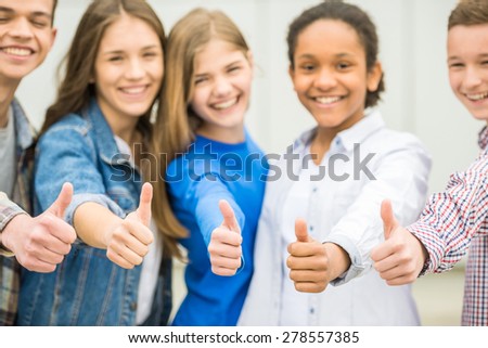 Group of smiling cheerful teenagers having fun after lessons and showing thumbs up.