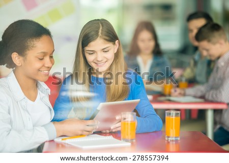 Two female friends sitting in cafe, using tablet and drinking orange juice.