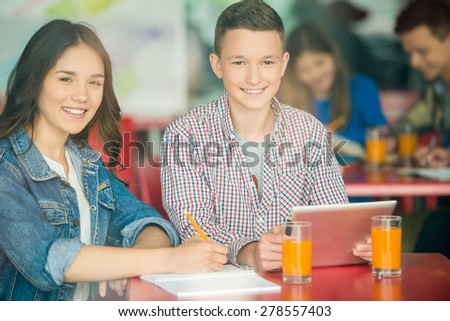 Two friends sitting in school cafe, studying and drinking orange juice.