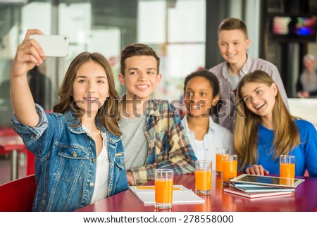 A group of teenagers sitting at the table in cafe, doing selfie and drinking orange juice.