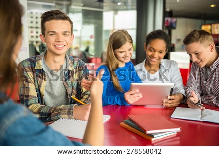 A group of teenagers sitting at the table in cafe, studying and using tablet.