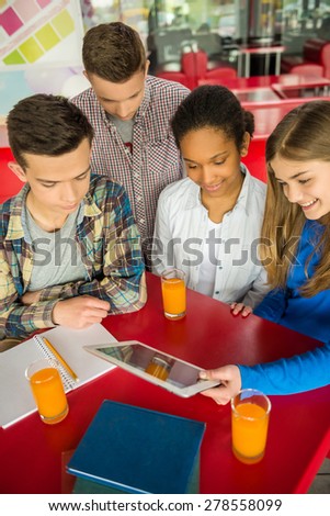 A group of teenagers sitting at the table in cafe, studying and drinking orange juice.