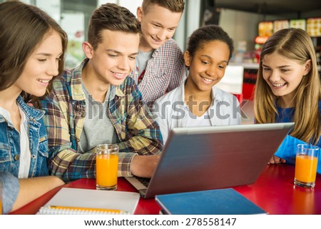 A group of teenagers sitting at the table in cafe, using laptop and drinking orange juice.