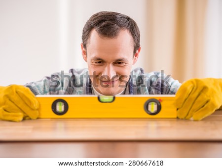 Image of smiling carpenter in rubber gloves measuring wooden plank.