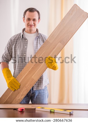 Image of smiling carpenter in rubber gloves holding wooden planks.