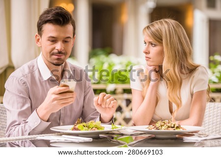 Young smiling couple in gorgeous restaurant. Man looking at phone.