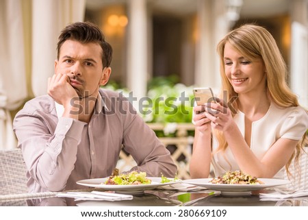 Man is getting bored in restaurant while his woman looking at phone.