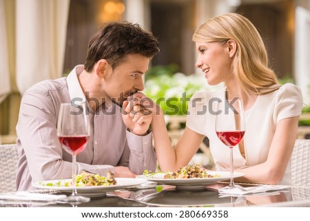 Young smiling couple enjoying the meal in gorgeous restaurant and drinking wine. Man kissing woman\'s hand.