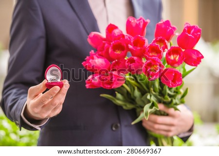 Close-up of man holding bouquet of tulips and gift box with ring. Proposal.