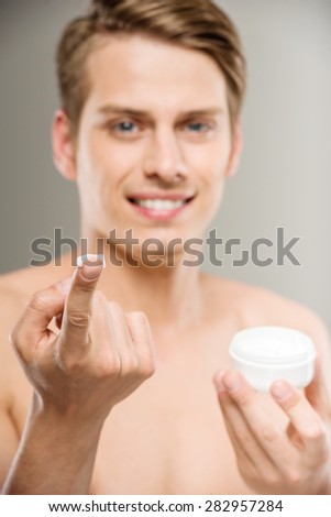 Portrait of young handsome man applying cream lotion on face.