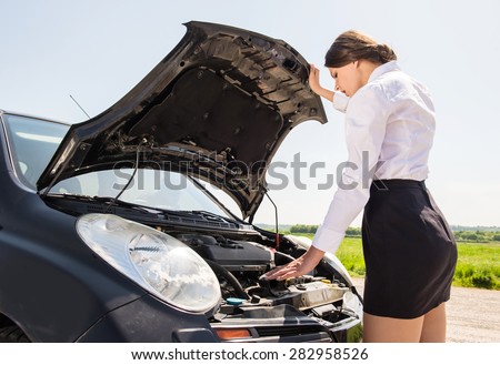 Beautiful businesswoman examining broken down car engine at countryside.