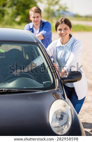 Young attractive couple pushing a car with empty fuel tank.