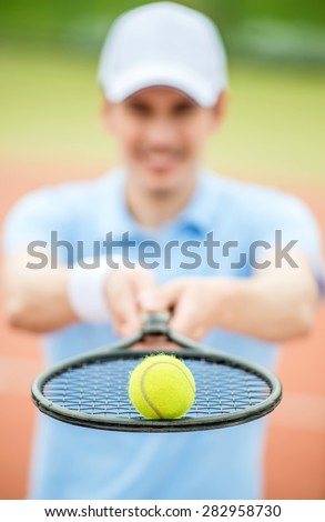 Handsome man stood in front of tennis court holding racket. Sport outdoors.