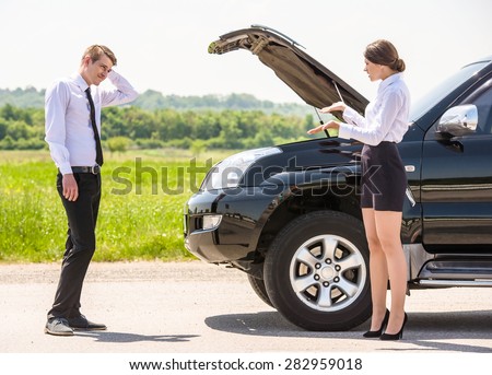 Young couple dressed formal having quarrel near a broken car on the roadside.