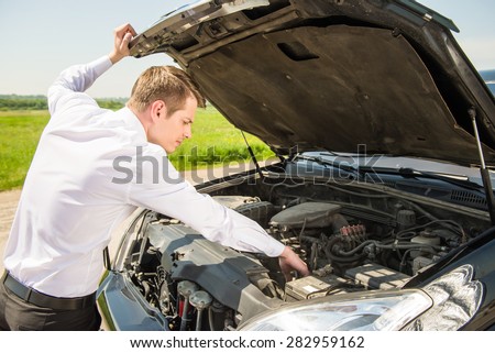 Side view of young businessman examining broken down car engine at countryside.