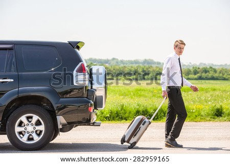 Full length side view of young businessman with suitcase leaving broken car at countryside.