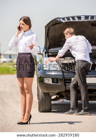Businessman trying to repair his broken car while his woman calling for help on phone.