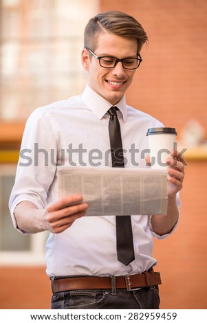 Confident manager dressed formal drinking coffee and holding newspaper outdoors.