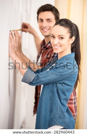 Happy young couple is measuring their new empty apartment. Repair and building concept.