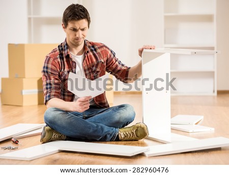 Concentrated young man reading the instructions to assemble furniture in the kitchen at home.