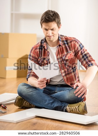 Concentrated young man reading the instructions to assemble furniture in the kitchen at home.